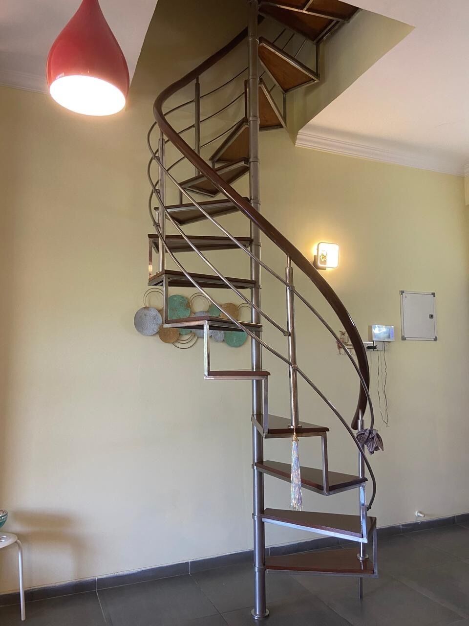 Una escalera de caracol con barandilla de metal y una lámpara colgante roja.