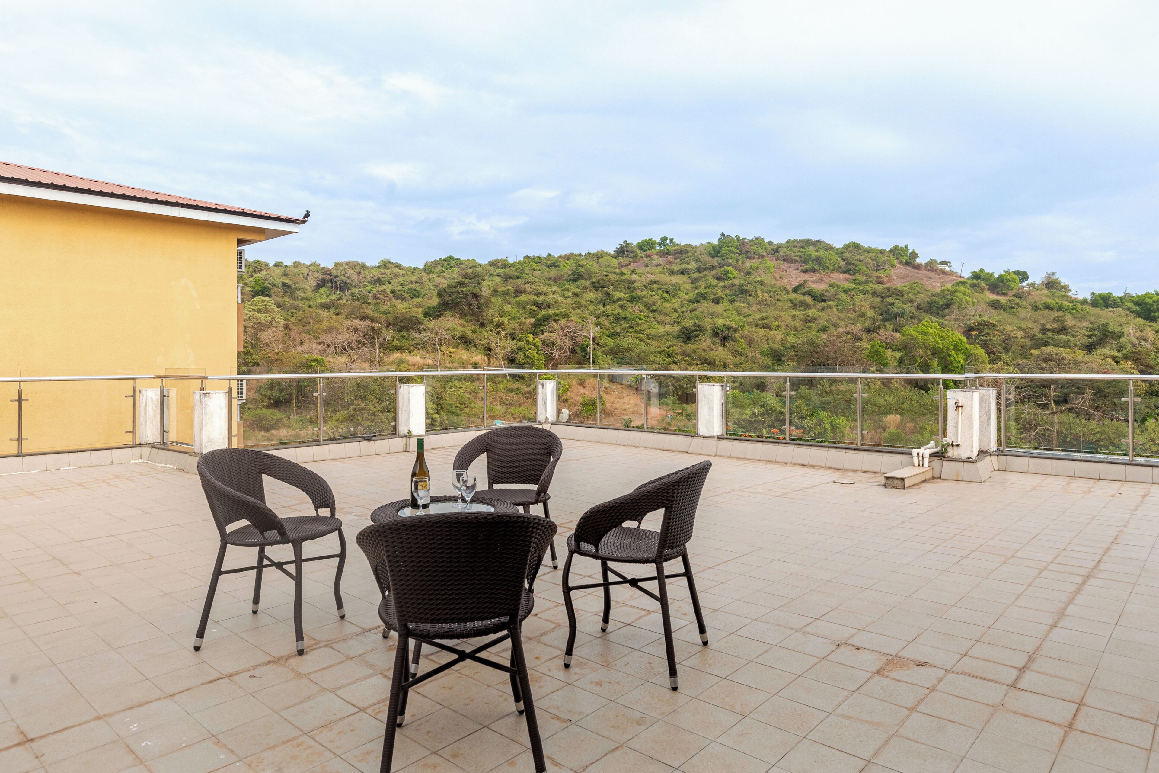 A terrace with four wicker chairs and a table, overlooking a hillside.