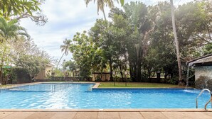 A swimming pool with a tiled deck, surrounded by lush greenery and trees. - Cinderella apartment with private sundeck candolim (Candolim)