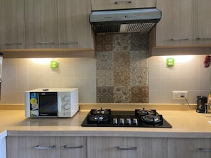 A kitchen with a microwave, gas stove, and wooden cabinets. - Cinderella apartment with private sundeck candolim (Candolim)