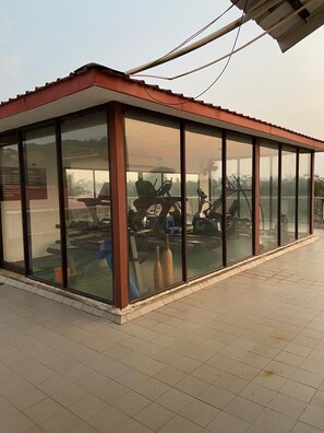 A glass-walled structure with exercise equipment inside, a tiled floor, and a red roof. - Cinderella apartment with private sundeck candolim (Candolim)