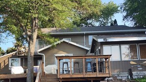 A two-story house with a wooden deck, a staircase, and a stone wall. - Spacious 6-bedroom house located on Richmond Lake. (Aberdeen)