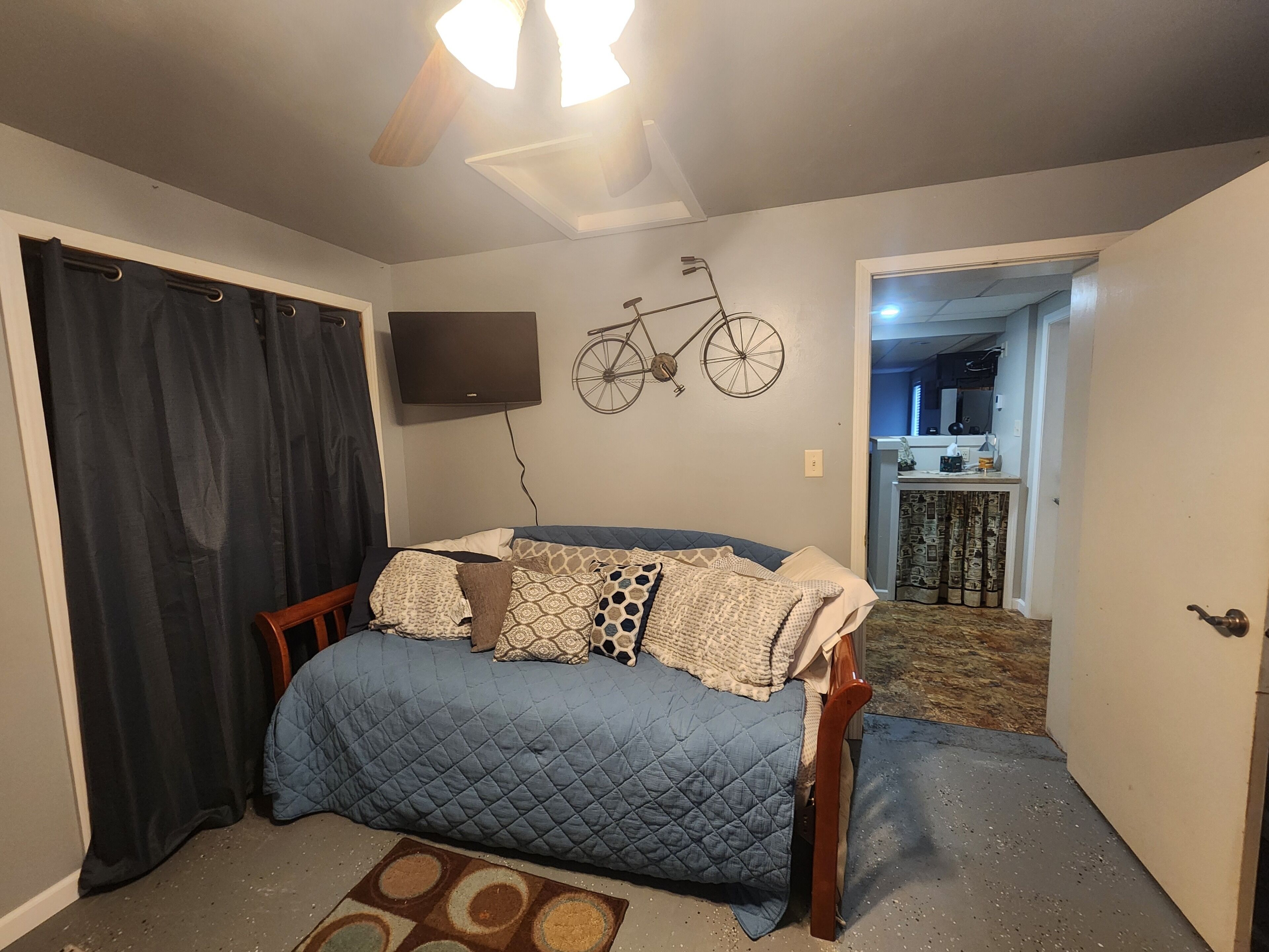 A bedroom with a bed, a ceiling fan, a mounted television, and a bicycle decoration on the wall.