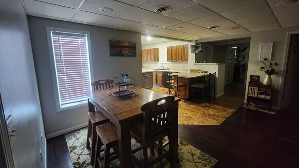 A dining area with a wooden table and chairs, a kitchen in the background, and a window with blinds. - Spacious 6-bedroom house located on Richmond Lake. (Aberdeen)