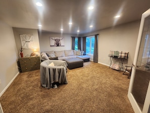 A living room with a sectional sofa, a small ottoman, a glass coffee table, and a decorative wall piece. - Spacious 6-bedroom house located on Richmond Lake. (Aberdeen)