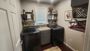 A laundry room with two front-loading washers, a drying rack, and shelves with various items. - Spacious 6-bedroom house located on Richmond Lake. (Aberdeen)