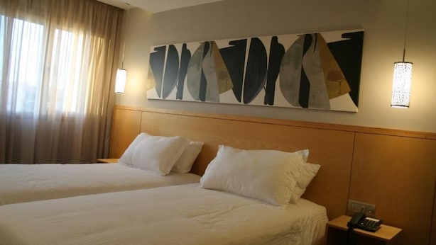 Una camera d'albergo con due letti, un quadro astratto di grandi dimensioni appeso al muro e un comodino con un telefono.