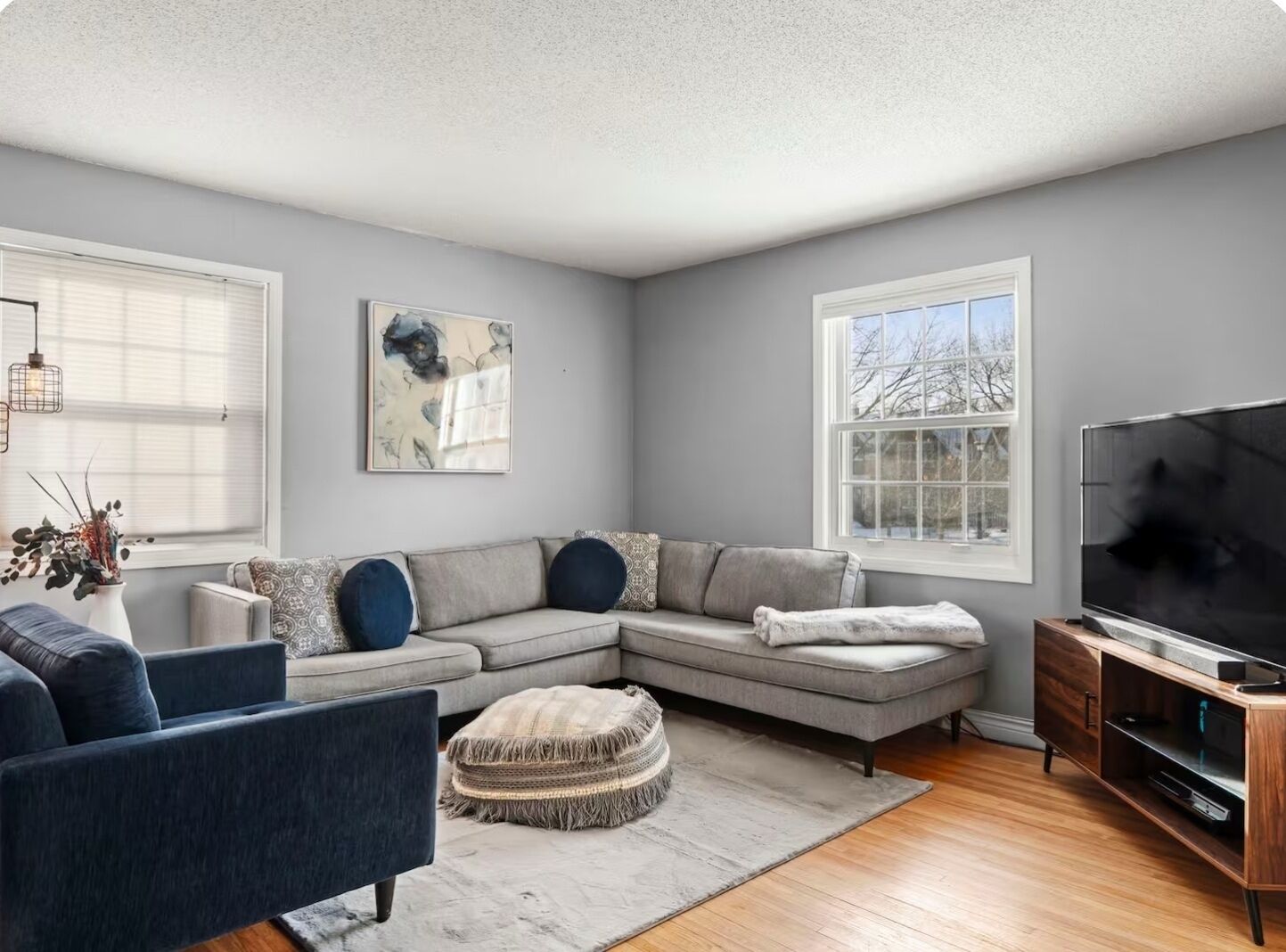 A modern living room with a sectional sofa, a flat-screen TV, and a large window providing a view of the outdoors.