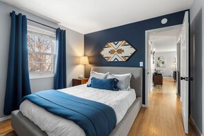 Ein Schlafzimmer mit Bett, Nachttisch, Lampe und einer geometrischen Wanddekoration.