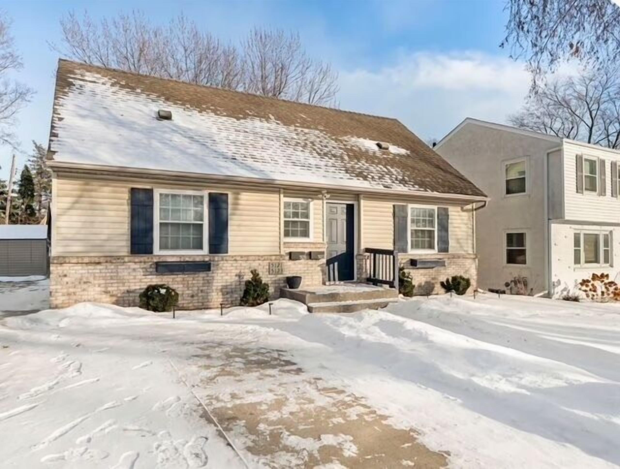 A two-story house with a front porch, a garage, and a snow-covered driveway.