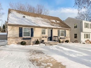 Une maison à deux étages avec un porche à l’avant, un garage et une allée recouverte de neige.