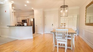 A spacious kitchen with white cabinetry, a central island, and a dining area with a wooden table and chairs. - Furnished Monthly Rental near Folly (Charleston)