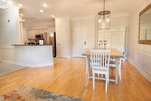 A spacious kitchen with white cabinetry, a central island, and a dining area with a wooden table and chairs. - Furnished Monthly Rental near Folly (Charleston)