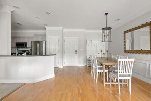 A modern kitchen with white cabinetry, a central island, and a dining area with a wooden table and white chairs. - Furnished Monthly Rental near Folly (Charleston)