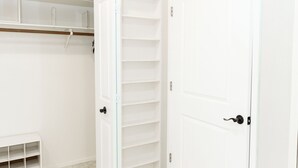 Um quarto com chão de azulejos brancos, uma porta branca e um armário branco com prateleiras.