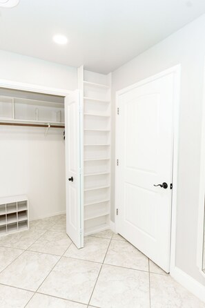 Ein Zimmer mit weiß gefliestem Boden, einer weißen Tür und einem weißen Kleiderschrank mit Regalen.