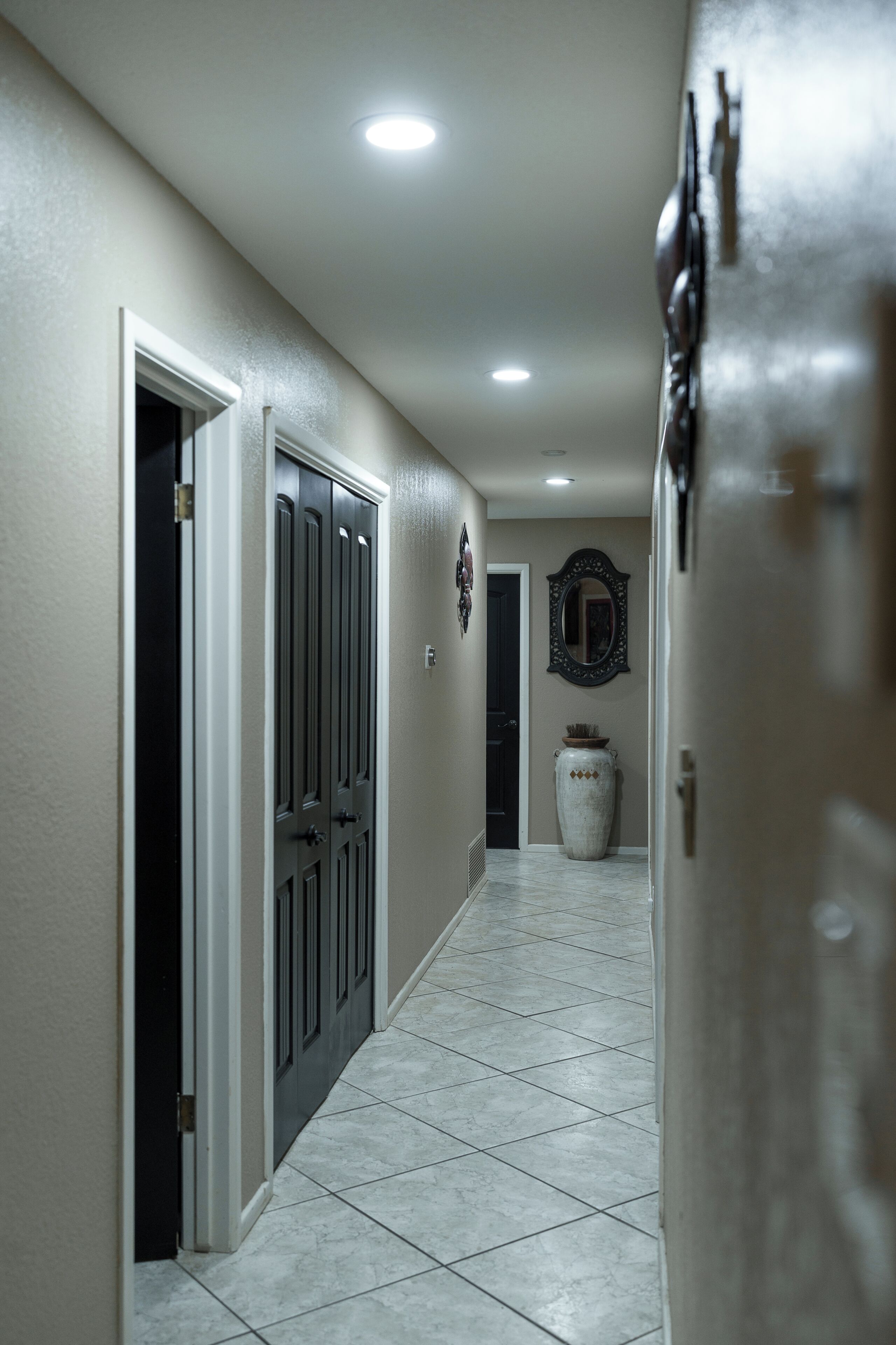 A hallway with a tiled floor, a door, a mirror, and a vase on the wall.