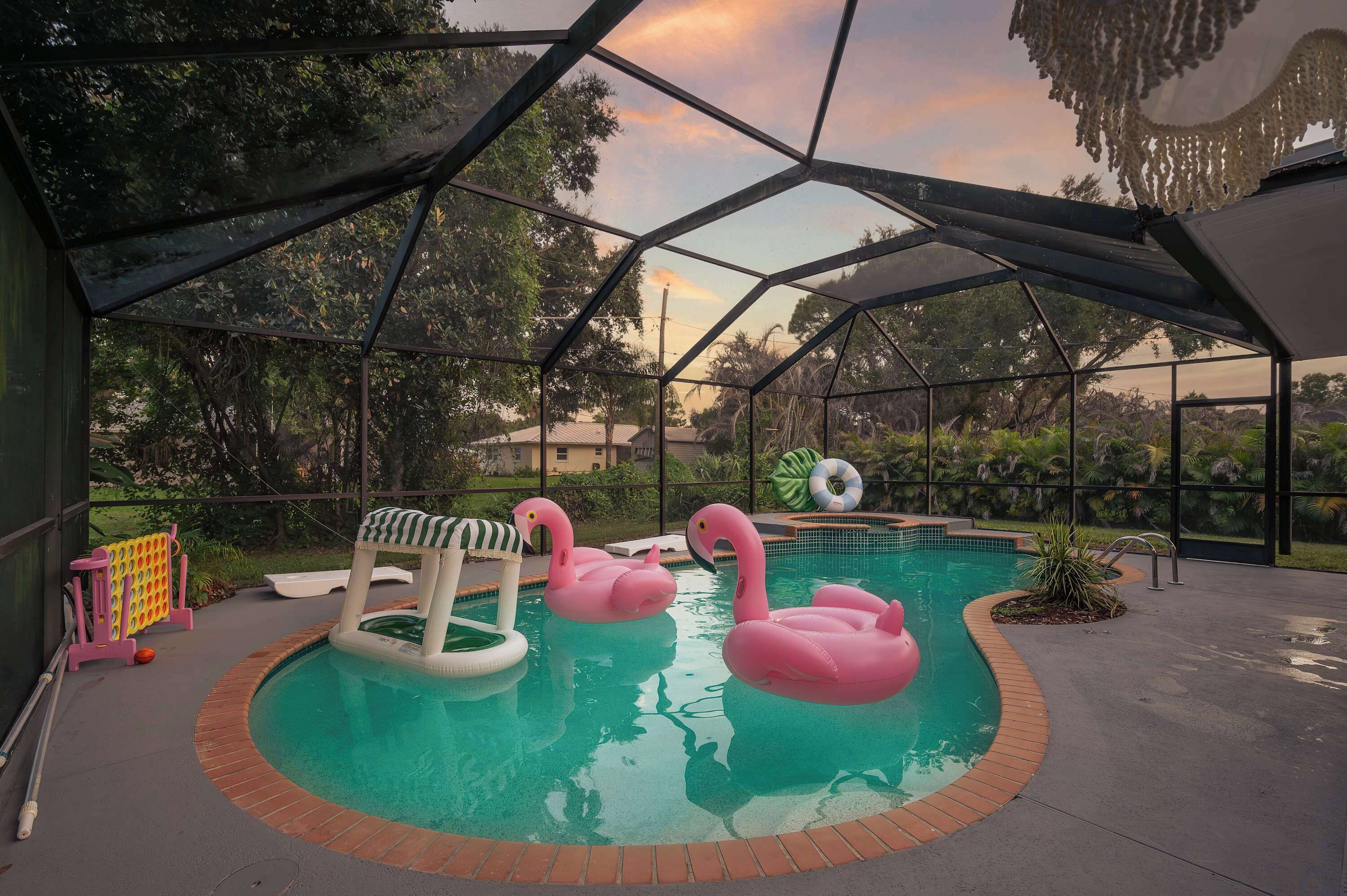 Een binnenzwembad met twee roze flamingo drijvers, een glijbaan en een zwembadterras met zonnescherm.