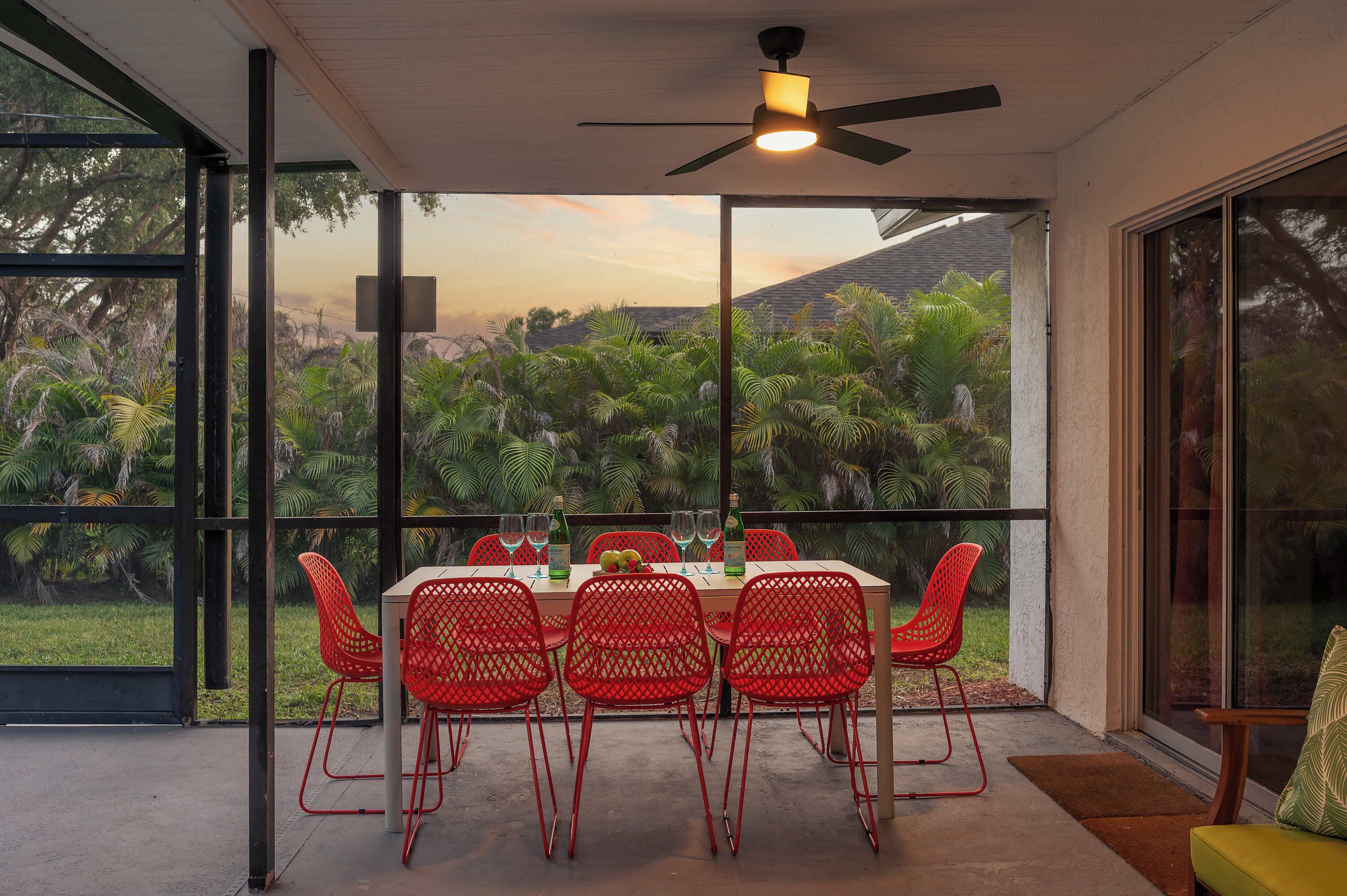 A dining area with a table set for six, surrounded by red chairs, overlooking a lush garden.