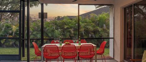 A dining area with a table set for six, surrounded by red chairs, overlooking a lush garden.