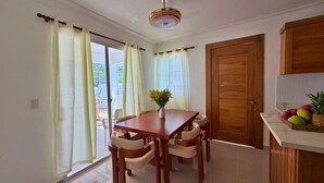 Ein Essbereich mit einem Holztisch und Stühlen, einer Blumenvase und Blick durch ein Fenster mit Vorhängen.