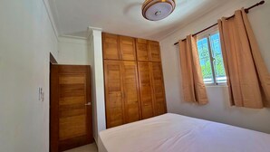 Ein Schlafzimmer mit Bett, Holzschrank und einem Fenster mit Vorhängen.