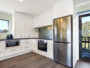 A modern kitchen with white cabinetry, stainless steel appliances, and a wooden floor. - Tepuia Cottage - Havelock Holiday Retreat (Picton)