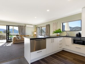 A modern kitchen with a central island, white cabinetry, and a view of the outdoors. - Tepuia Cottage - Havelock Holiday Retreat (Picton)