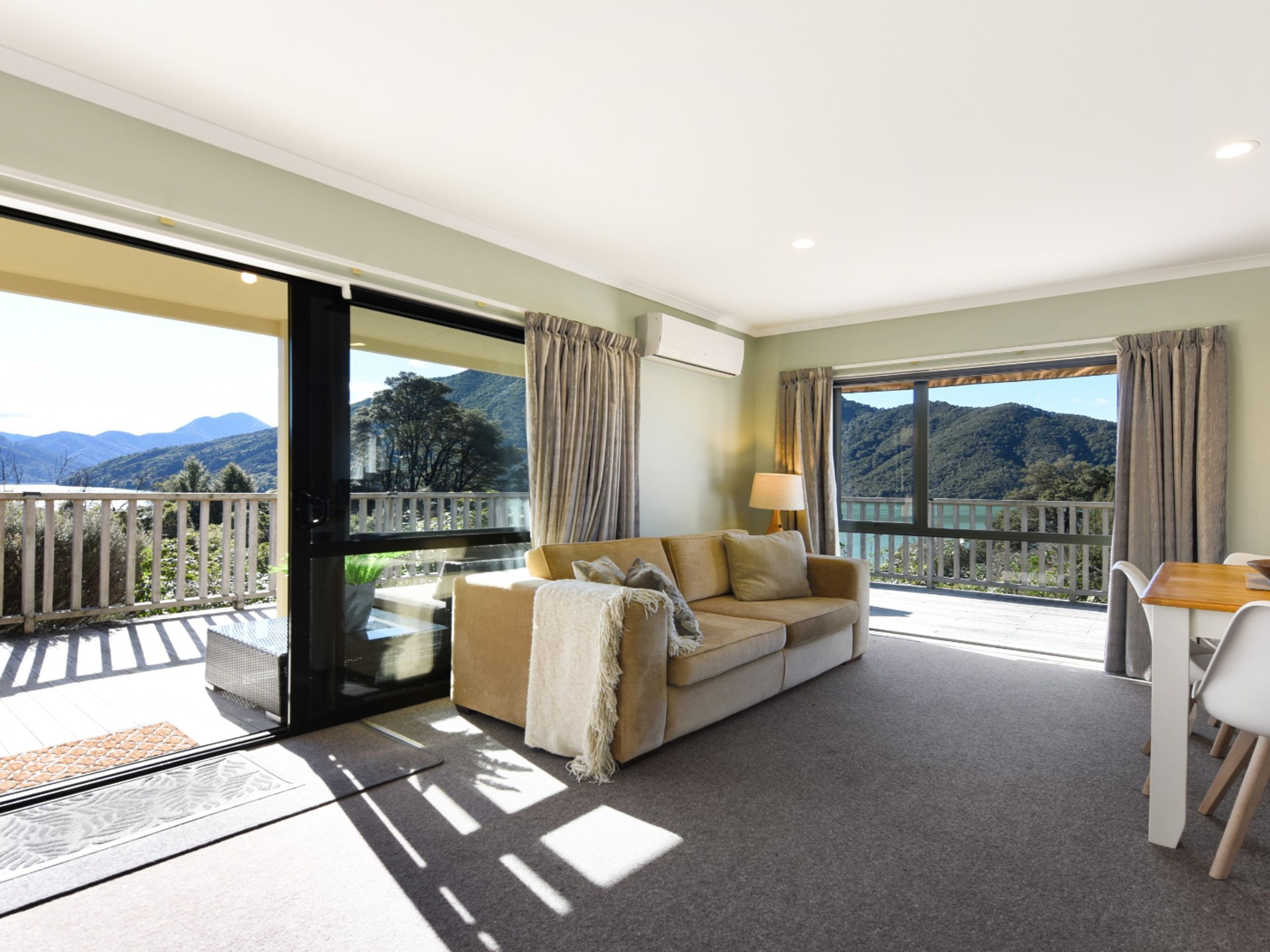A room with a sofa, a dining table, and a view of mountains through large windows.