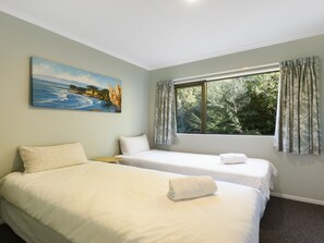 Une chambre avec deux lits, un tableau, une fenêtre avec des rideaux et une vue sur la verdure.