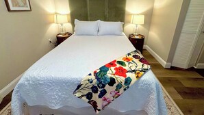 Ein ordentlich bezogenes Bett mit einer floralen Tagesdecke, zwei Nachttischlampen und einem gerahmten Bild an der Wand.