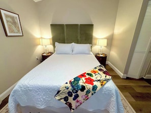 Ein ordentlich bezogenes Bett mit einer floralen Tagesdecke, zwei Nachttischlampen und einem gerahmten Bild an der Wand.