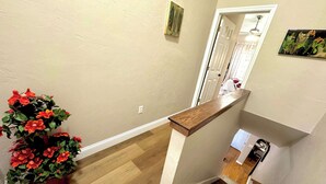 Eine Treppe mit einem Holzgeländer, ein Blumentopf mit roten Blüten und eine weiße Tür im Hintergrund.