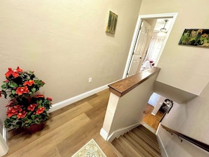 Eine Treppe mit einem Holzgeländer, ein Blumentopf mit roten Blüten und eine weiße Tür im Hintergrund.