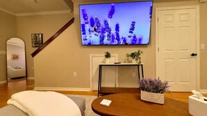 Ein Wohnzimmer mit einem an der Wand befestigten Flachbildfernseher, einem Holztisch, einer Couch und einer Tür.
