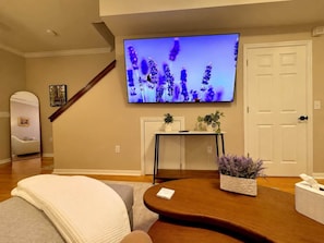 Ein Wohnzimmer mit einem an der Wand befestigten Flachbildfernseher, einem Holztisch, einer Couch und einer Tür.