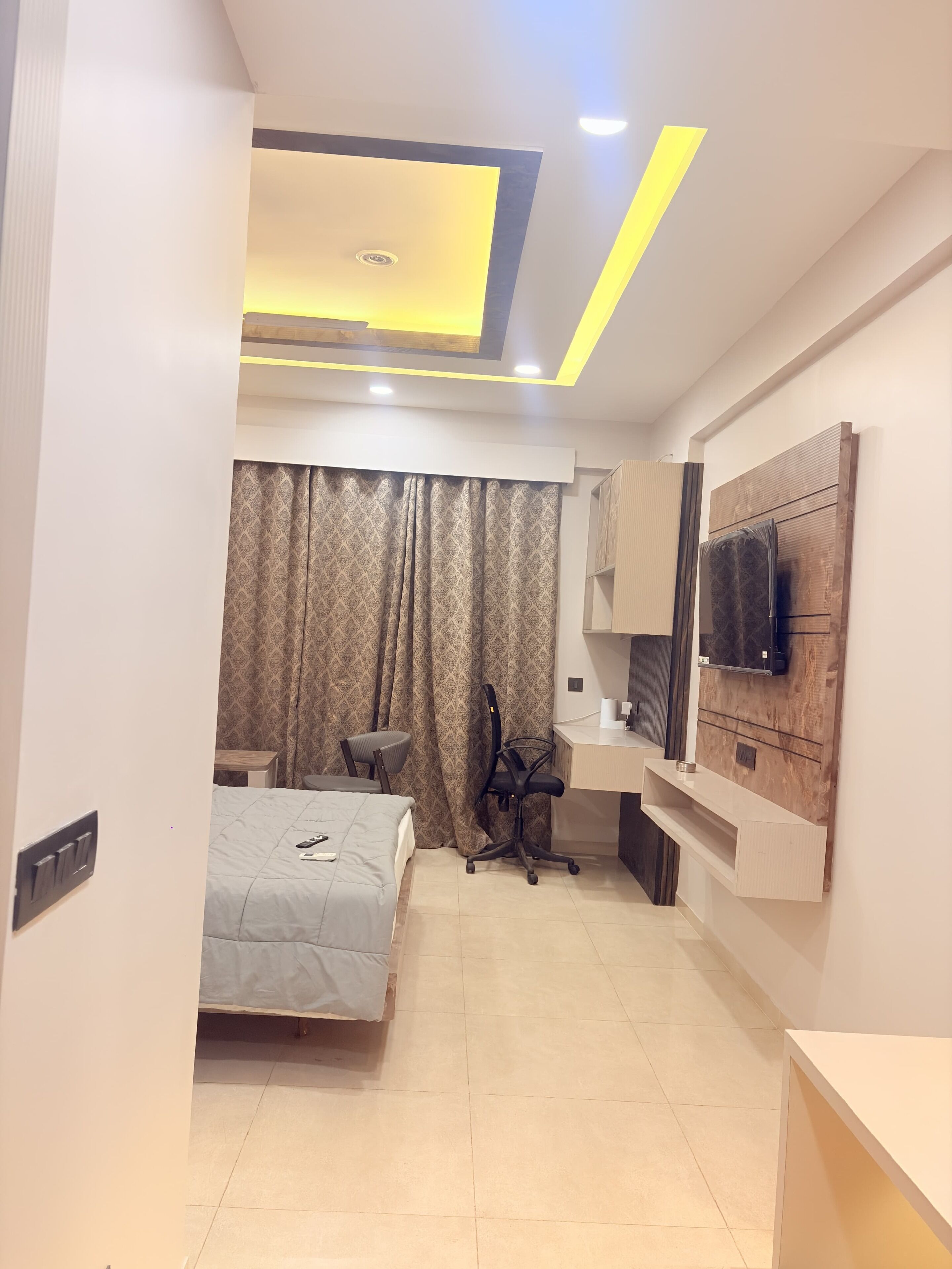 A hotel room with a bed, desk, chair, and a TV mounted on the wall.