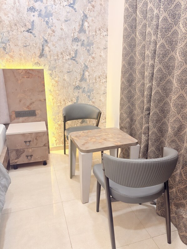 A room with a wooden table and two chairs, a sofa, and a patterned curtain.