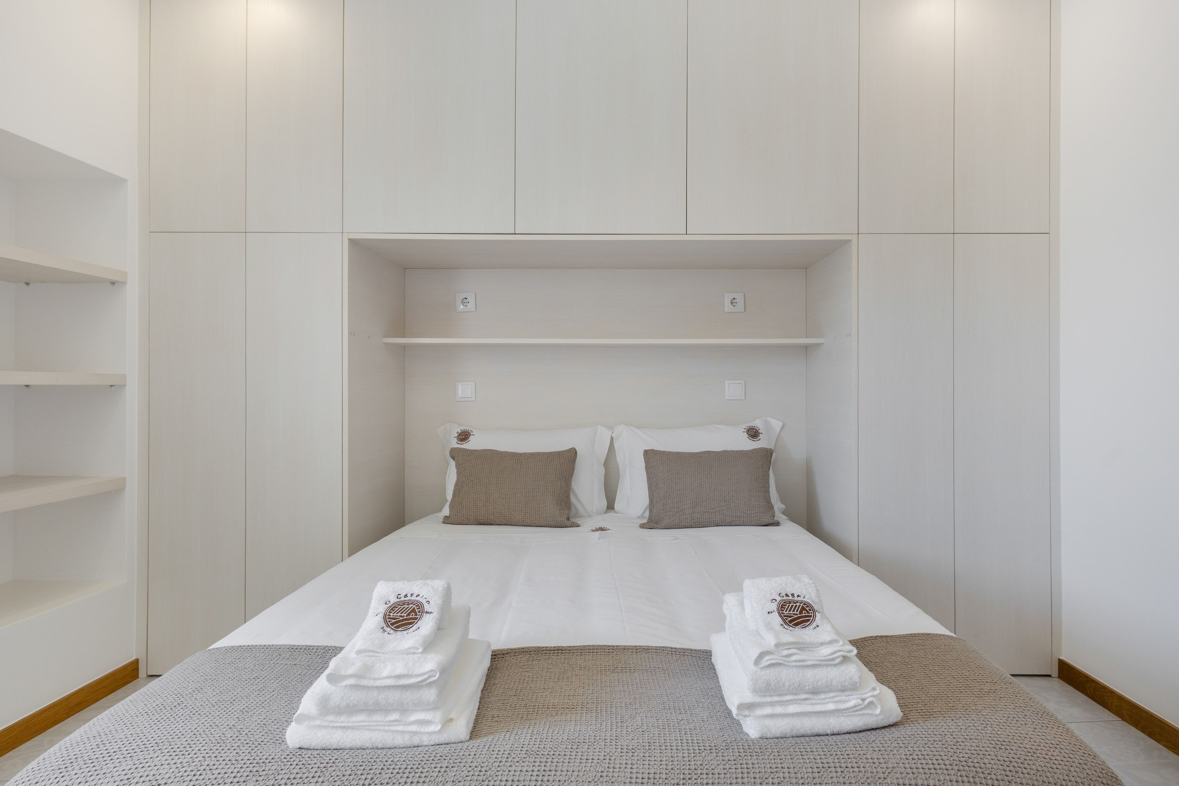A hotel room with a bed, two pillows, a white duvet, and two towels with a logo.