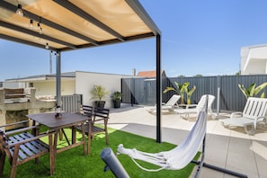 A covered outdoor patio with a table and chairs, a hammock, and a grill area.