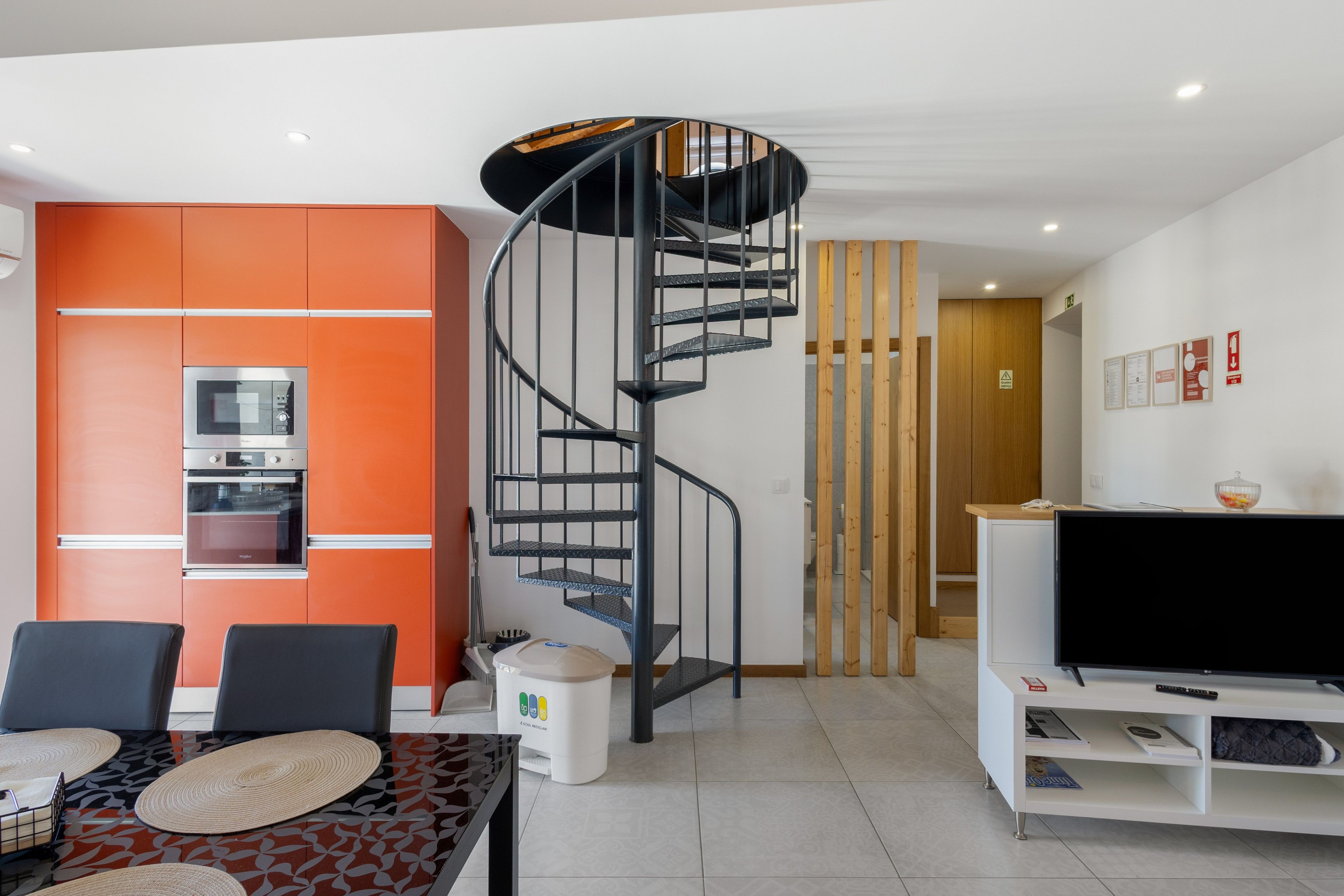 Una sala moderna con una escalera en espiral, un comedor y una cocina con armarios naranjas.