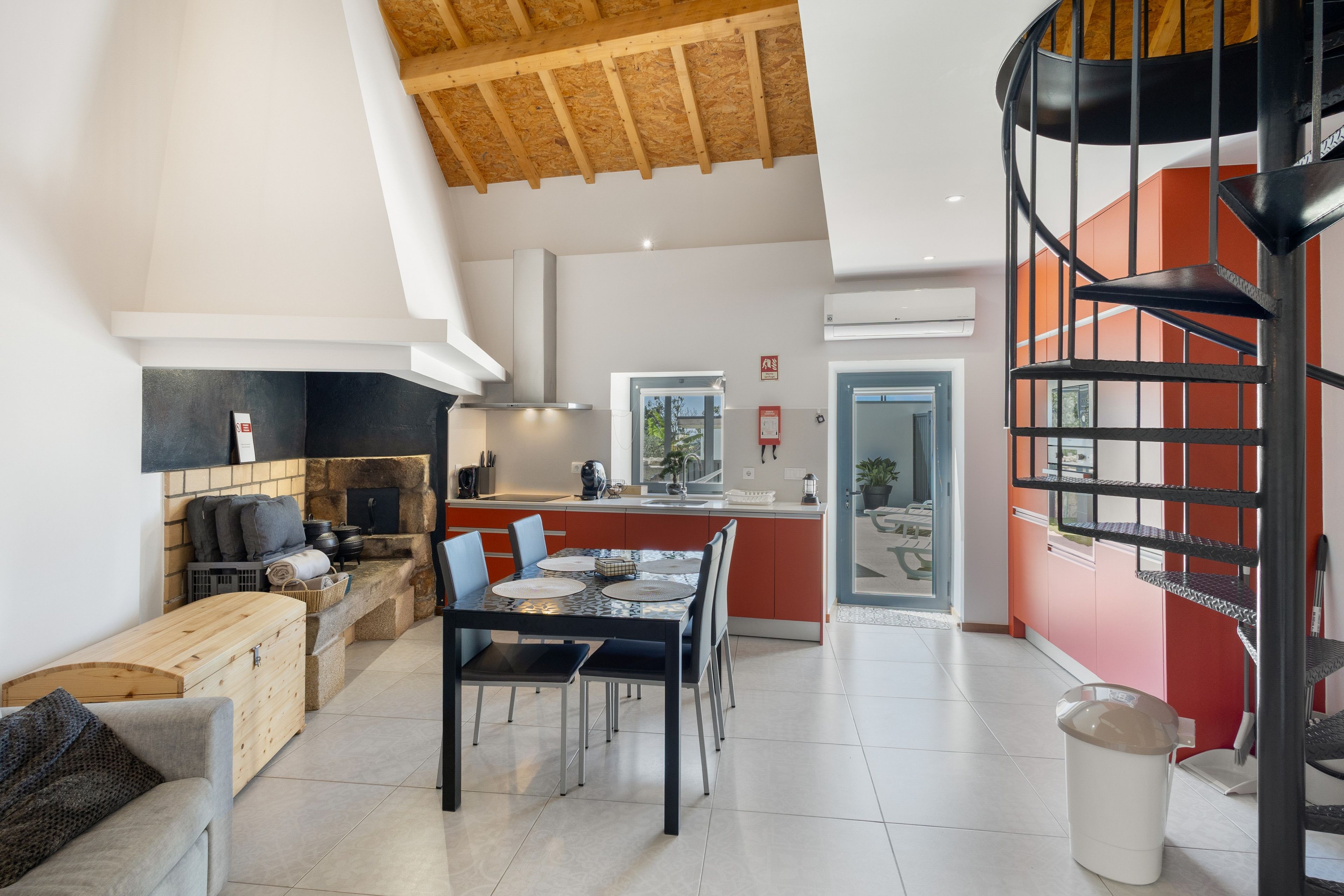 A modern kitchen with a central island, a dining area with chairs, a fireplace, and a spiral staircase.