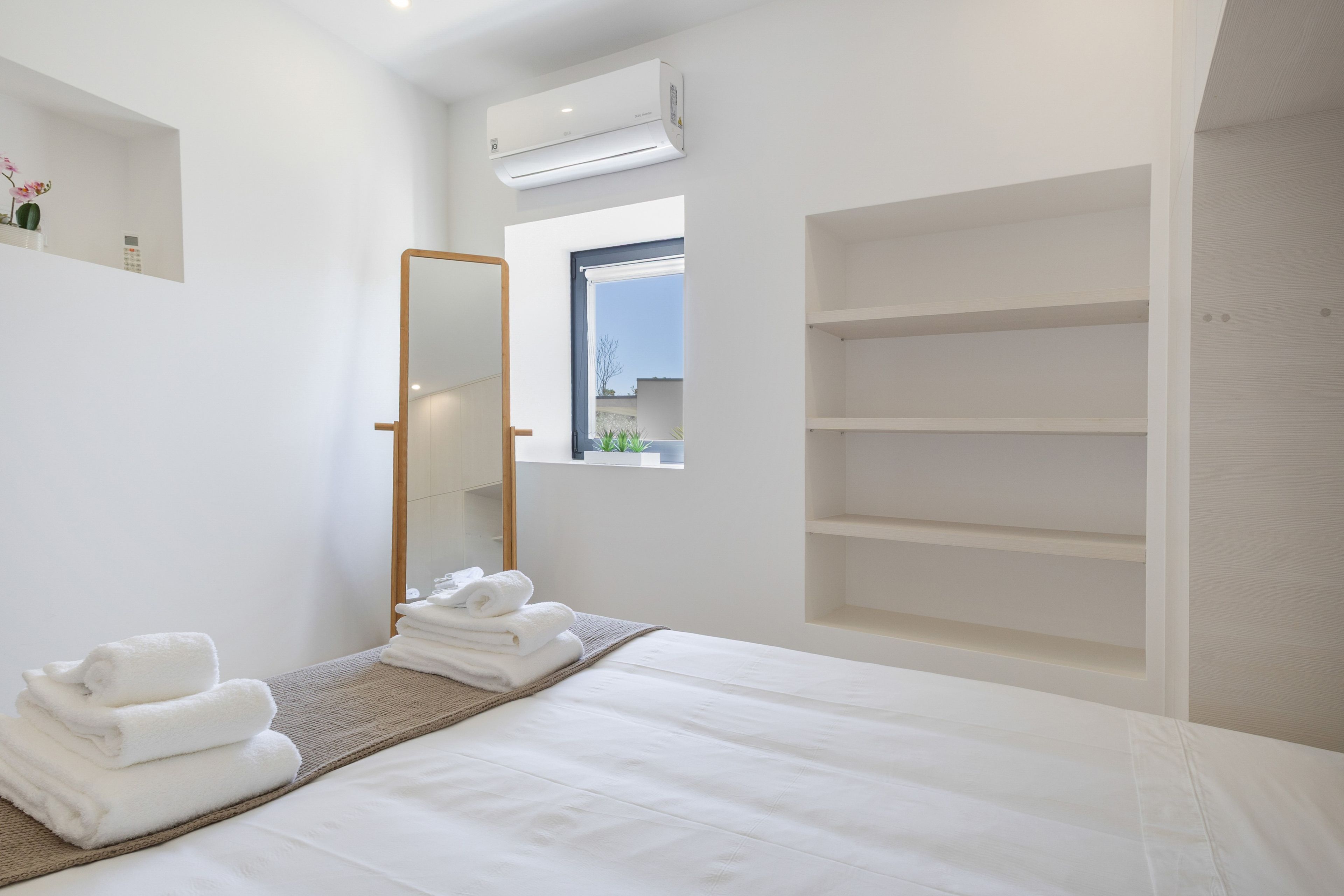 Un dormitorio moderno con una cama, un espejo grande, una ventana y estanterías empotradas.