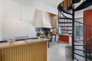 A modern kitchen with a central island, a dining area with chairs, and a spiral staircase.