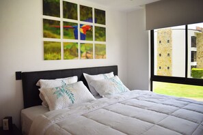 A bedroom with a large bed, a window with a view of a building, and a series of framed pictures on the wall. - Aparmet, 2 bedrooms, gym, pool, restaurant, tennis, hot tub, Rio Oro de Santa Ana (Río Oro)