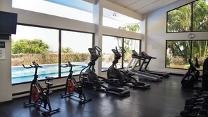 Ein Fitnessraum mit Trainingsgeräten, großen Fenstern und Blick auf einen Pool.