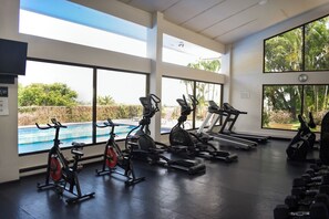 Ein Fitnessraum mit Trainingsgeräten, großen Fenstern und Blick auf einen Pool.