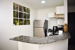 A modern kitchen with a granite countertop, stainless steel refrigerator, and a coffee maker. - Aparmet, 2 bedrooms, gym, pool, restaurant, tennis, hot tub, Rio Oro de Santa Ana (Río Oro)