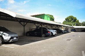 A parking area with multiple cars, a covered structure, and a green building in the background. - Aparmet, 2 bedrooms, gym, pool, restaurant, tennis, hot tub, Rio Oro de Santa Ana (Río Oro)