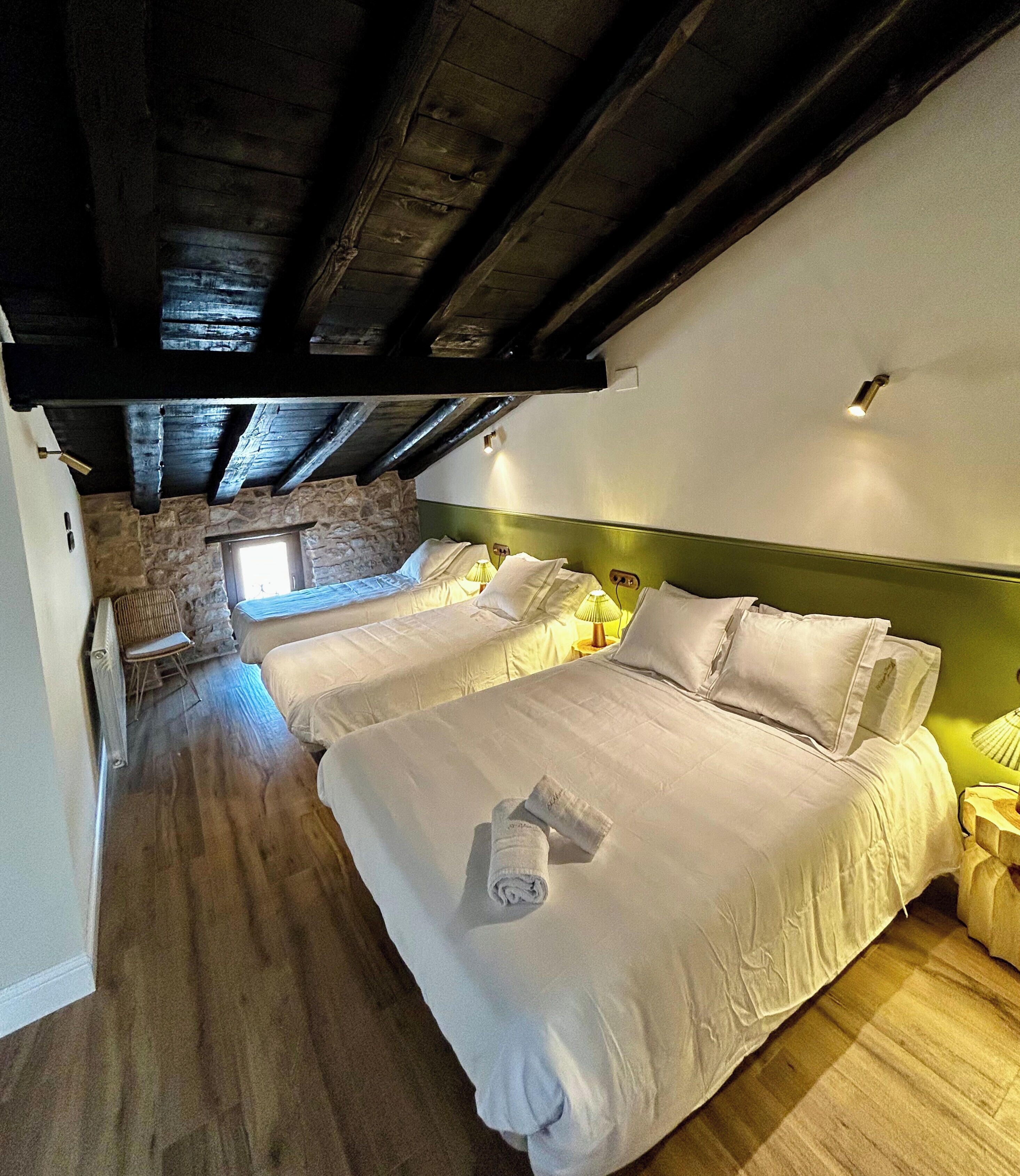 A hotel room with two beds, a stone wall, and a wooden ceiling.